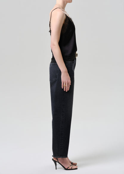 Person wearing a black sleeveless top and dark jeans on a grey background