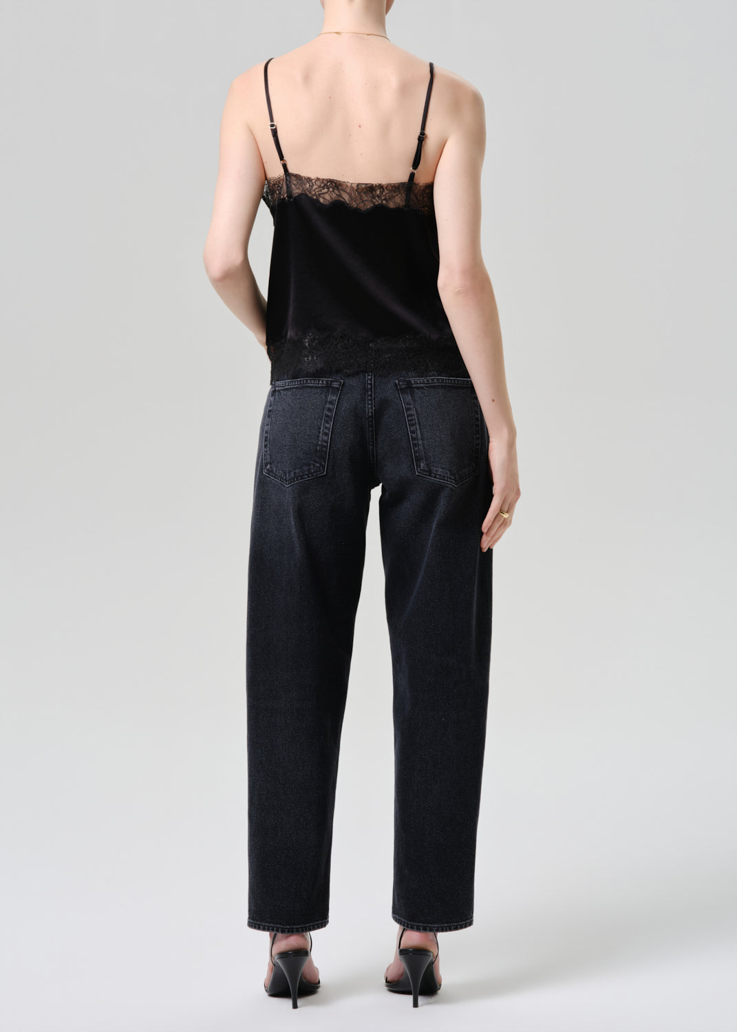 Person wearing a black lace top and dark jeans on a grey background