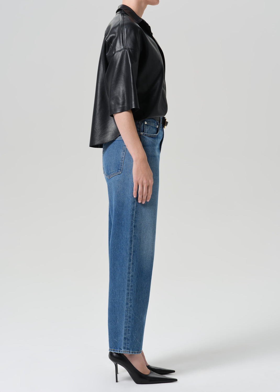 Person wearing black shirt with blue jeans on a grey background