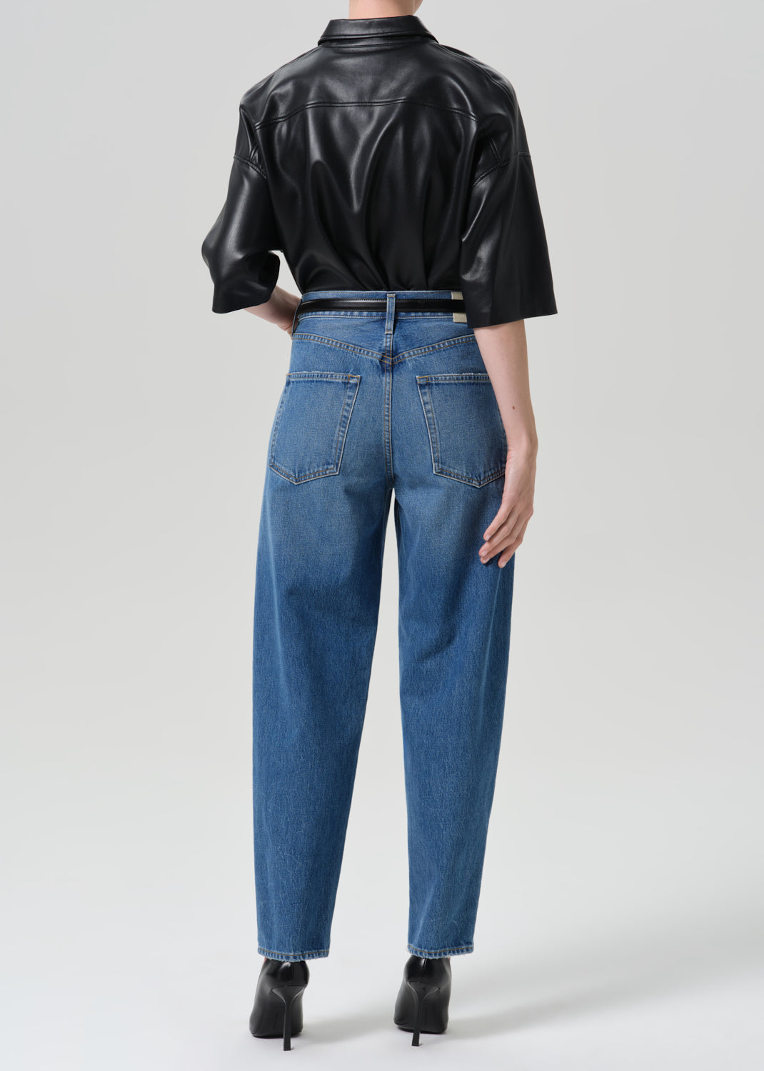 Person wearing black shirt with blue jeans on a grey background