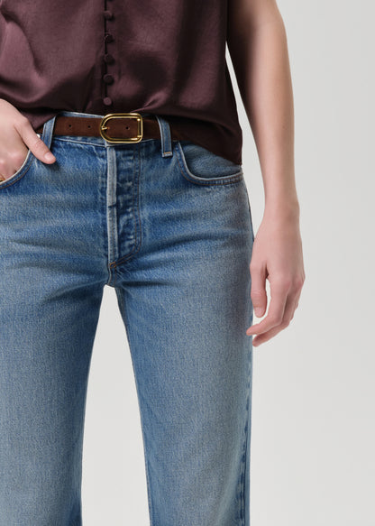 Person wearing blue jeans with a brown belt on a grey background