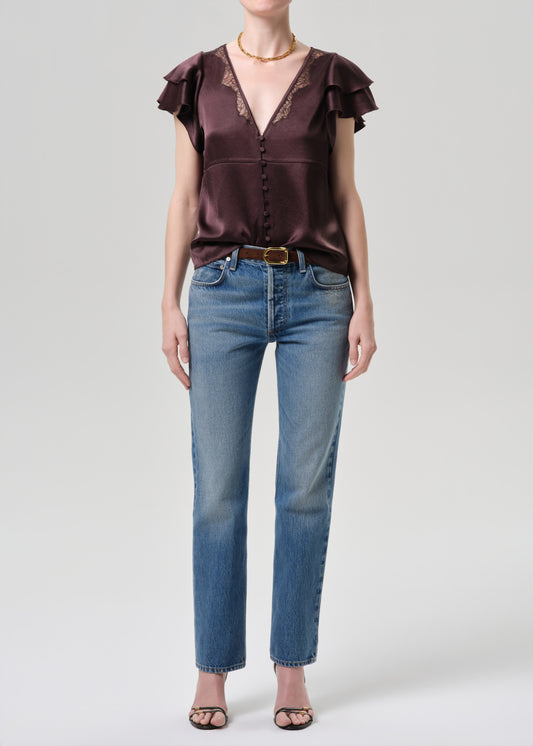 Woman wearing a brown satin blouse with ruffled sleeves and blue jeans on a grey background