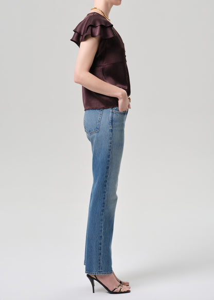 Person wearing a brown top with ruffled sleeves and blue jeans on a grey background