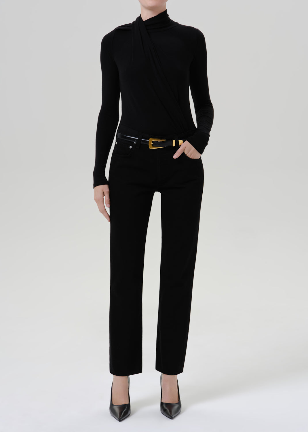 Person wearing a black fitted turtleneck with black straight leg pants on a grey background