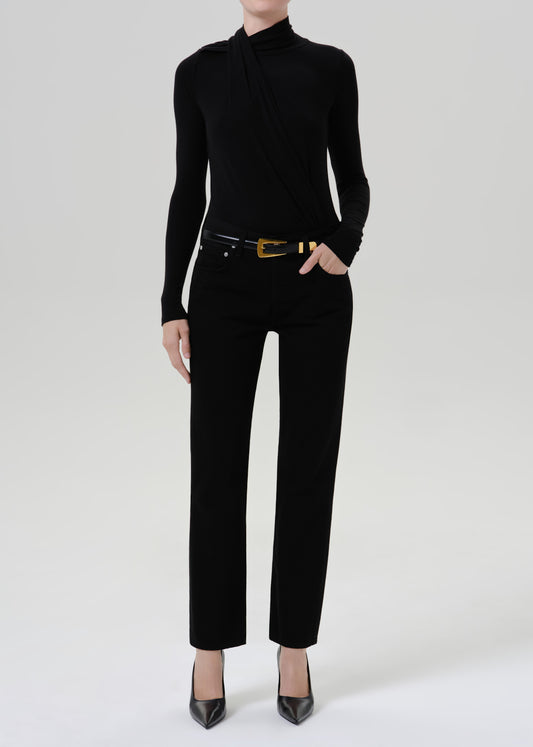 Person wearing a black fitted turtleneck with black straight leg pants on a grey background