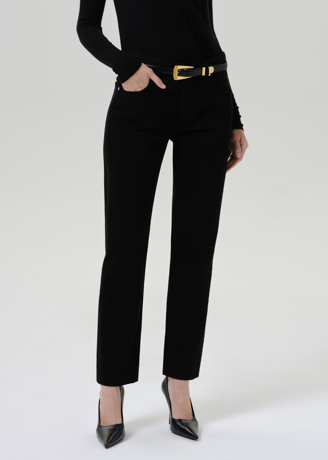 Person wearing a black fitted turtleneck with black straight leg pants on a grey background