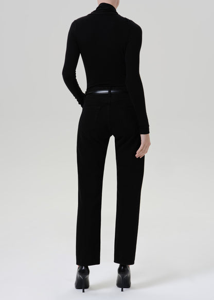 Person wearing a black fitted turtleneck with black straight leg pants viewed from the back on a grey background