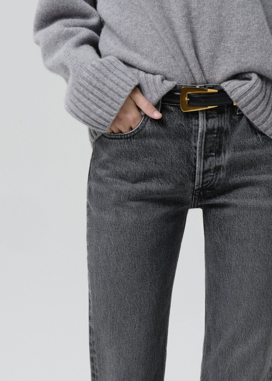 Close-up of grey straight leg jeans with a grey turtleneck sweater on a grey background