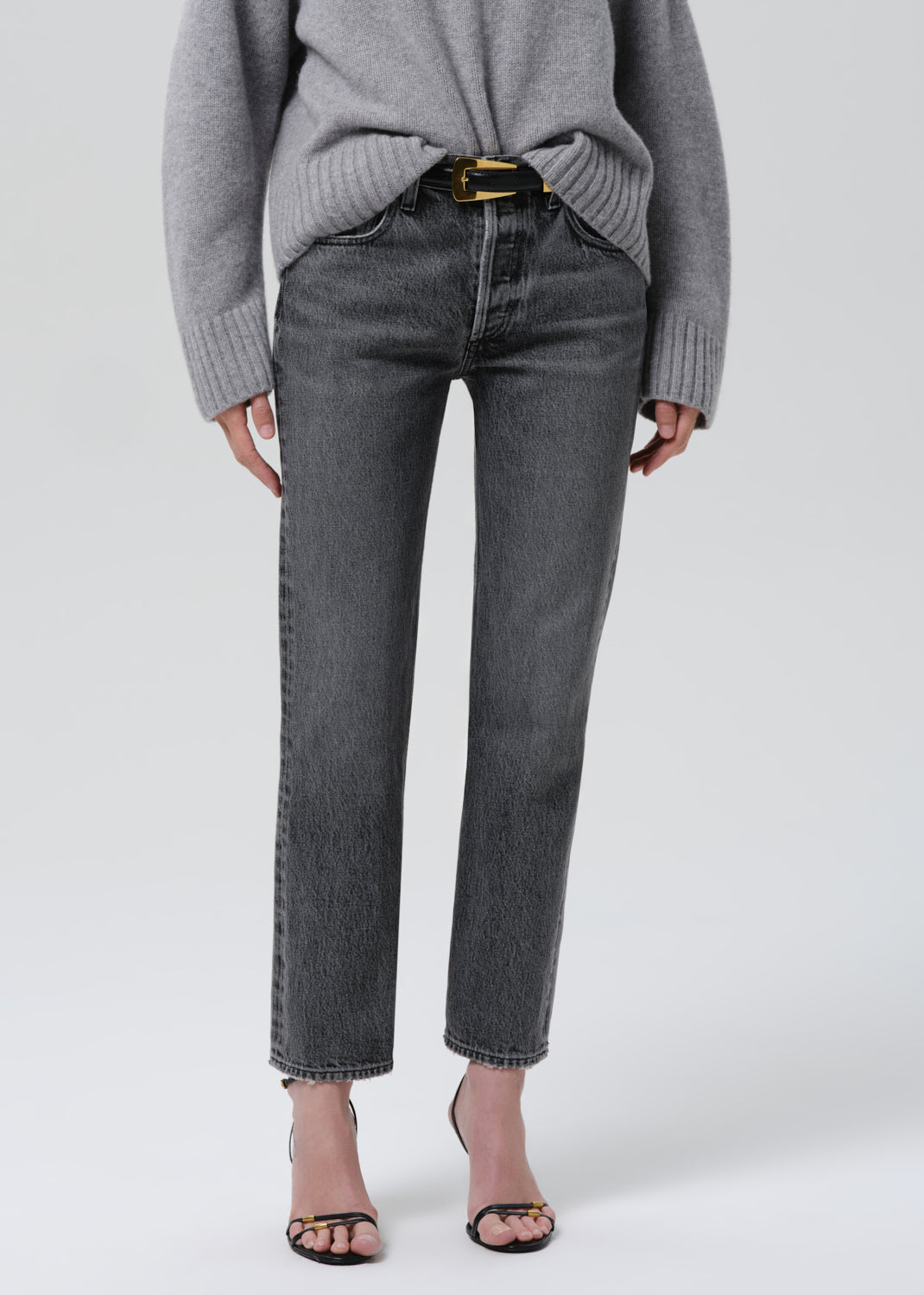 Person wearing a grey turtleneck sweater with grey straight leg jeans on a grey background