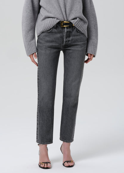 Person wearing a grey turtleneck sweater with grey straight leg jeans on a grey background