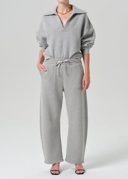 A model wearing a light grey two-piece loungewear set consisting of a half-zip sweatshirt and matching wide-leg sweatpants, photographed against a grey background.