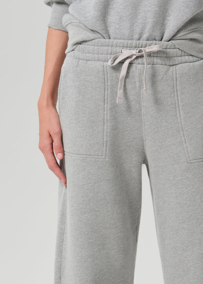 Close-up of a person wearing light grey heather sweatpants with a drawstring waist and front patch pockets, paired with a matching grey sweatshirt.