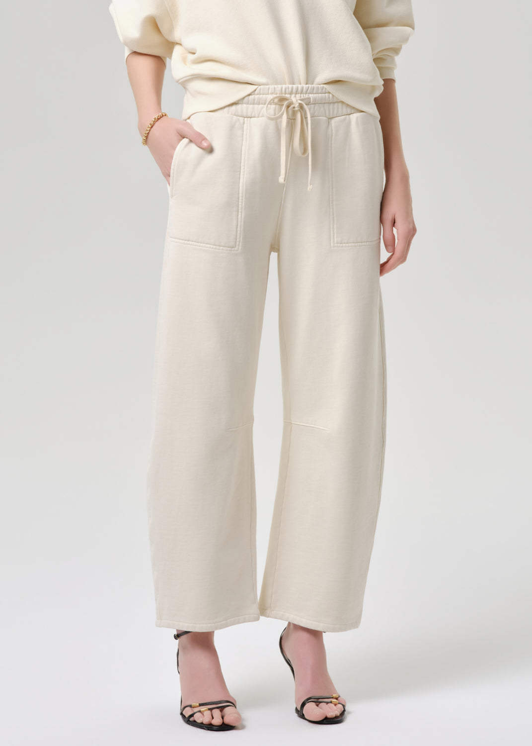 Person wearing cream-colored pants and a matching top on a grey background