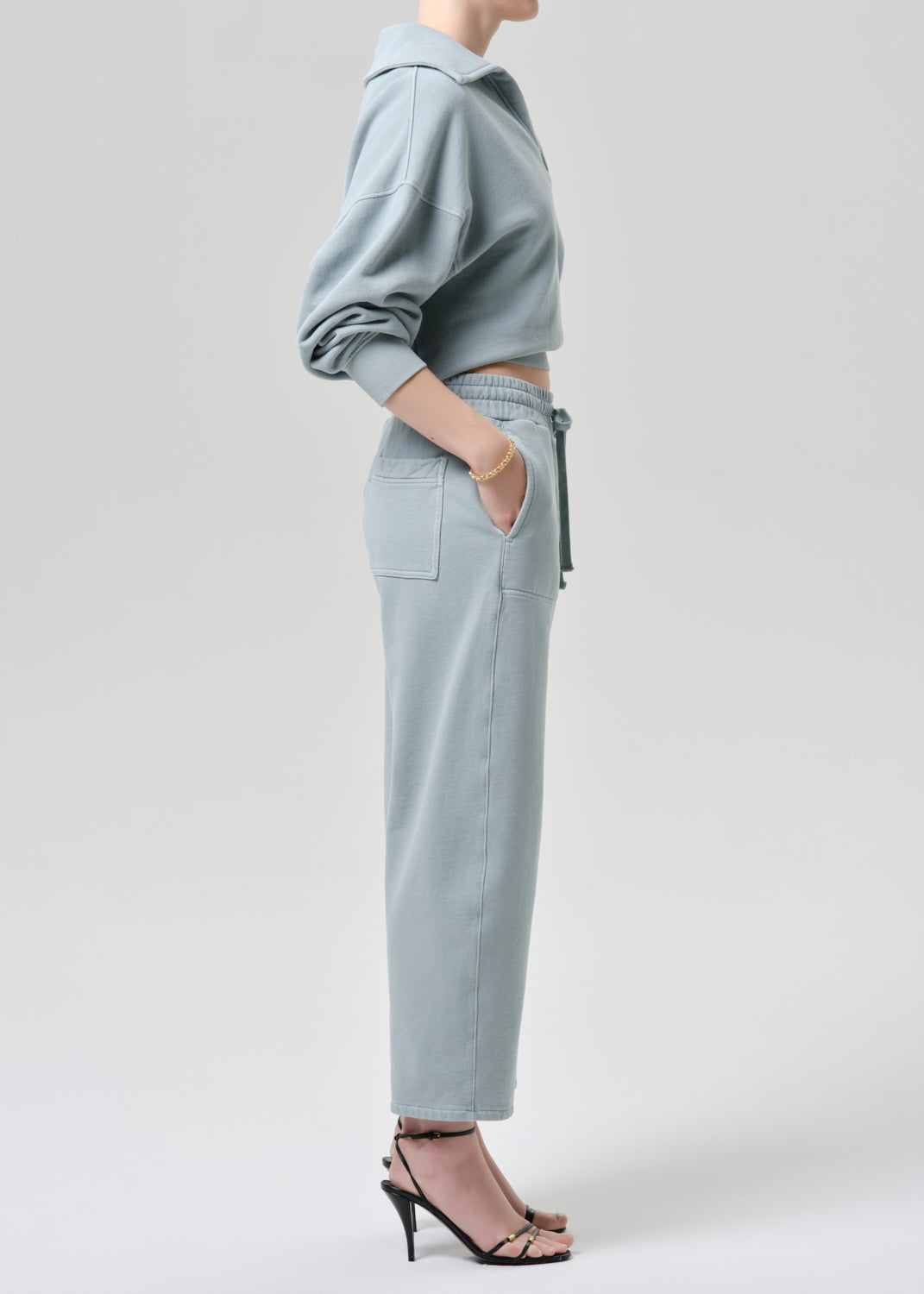 Person wearing a light blue outfit with a cropped top and high-waisted pants on a grey background