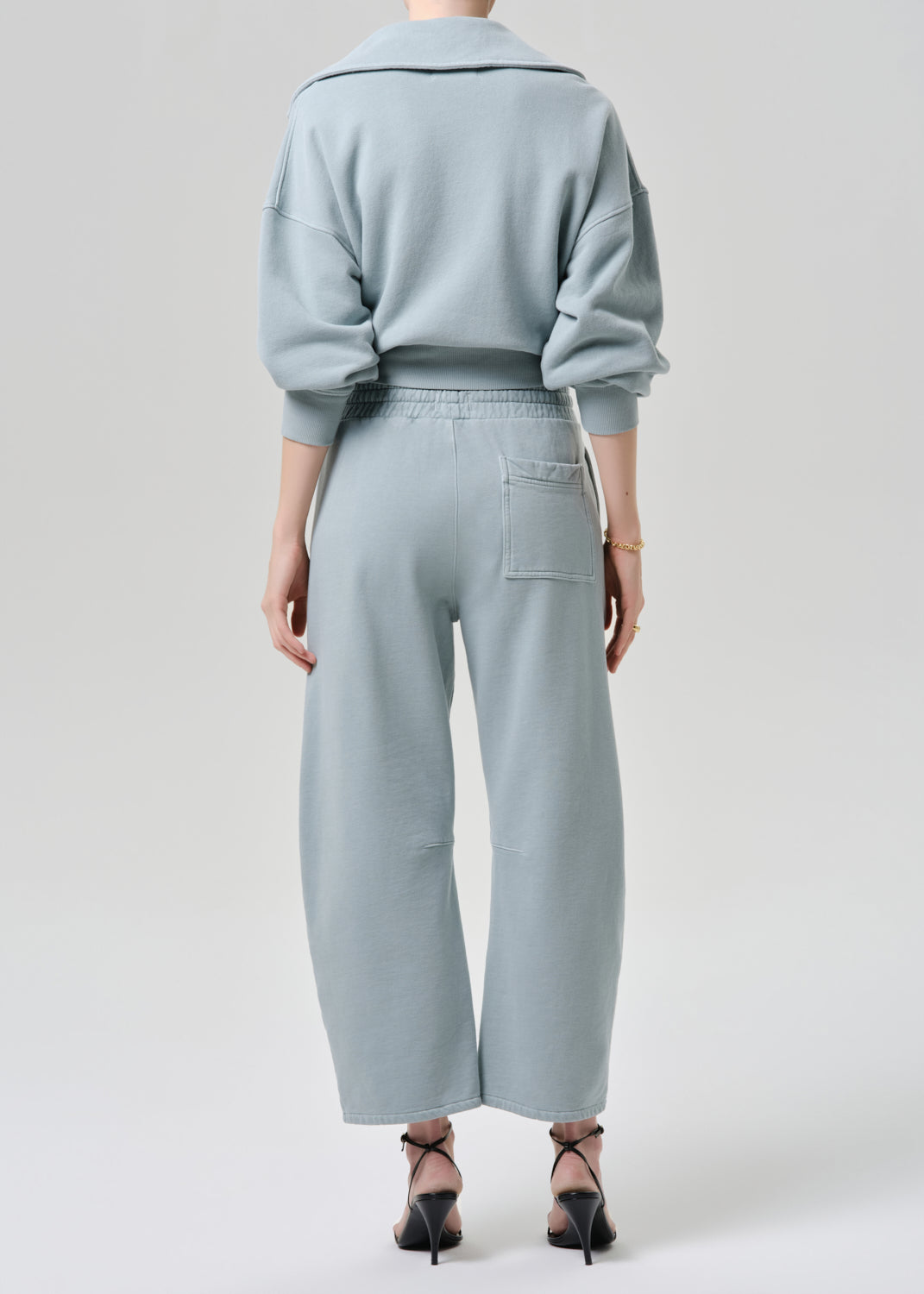 Person wearing a light blue outfit with a sweater and pants on a grey background
