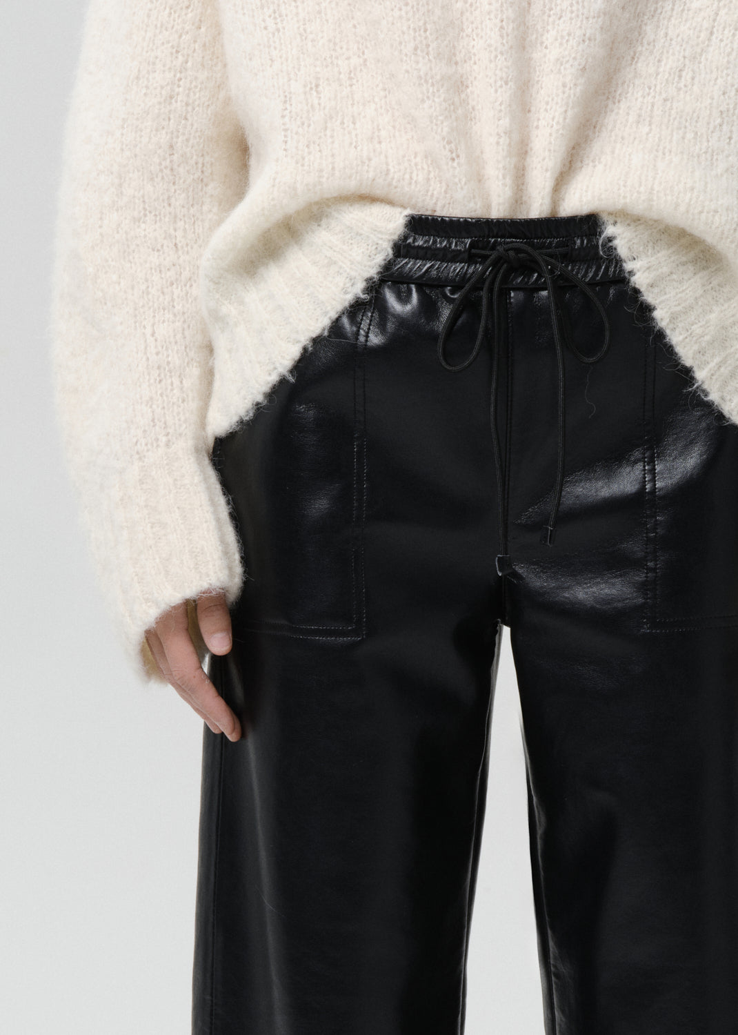 Person wearing a cream sweater and black leather pants on a grey background