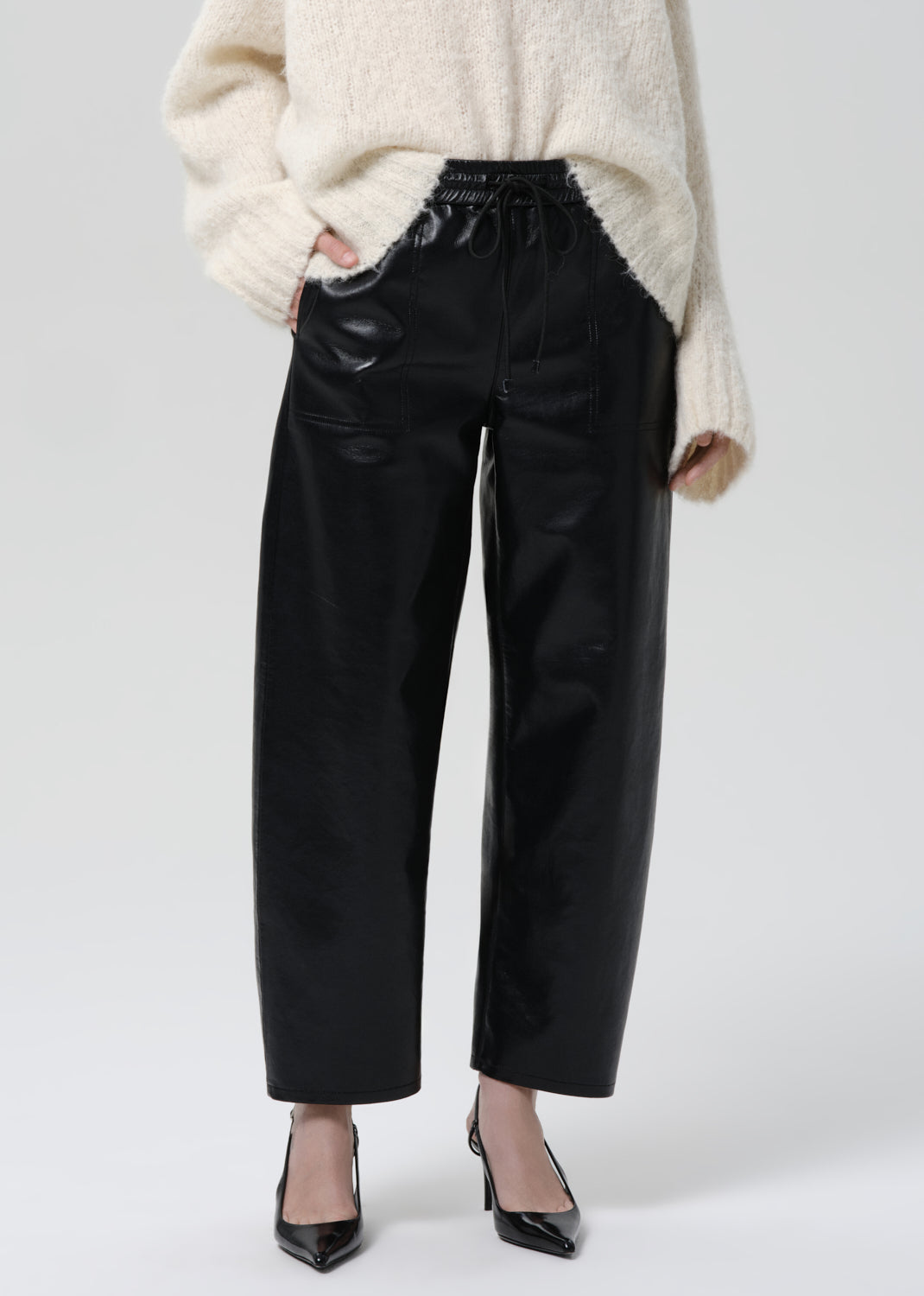 Person wearing a white sweater and black pants on a grey background