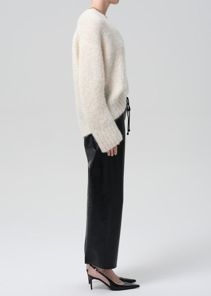 Person wearing a white sweater and black pants on a grey background