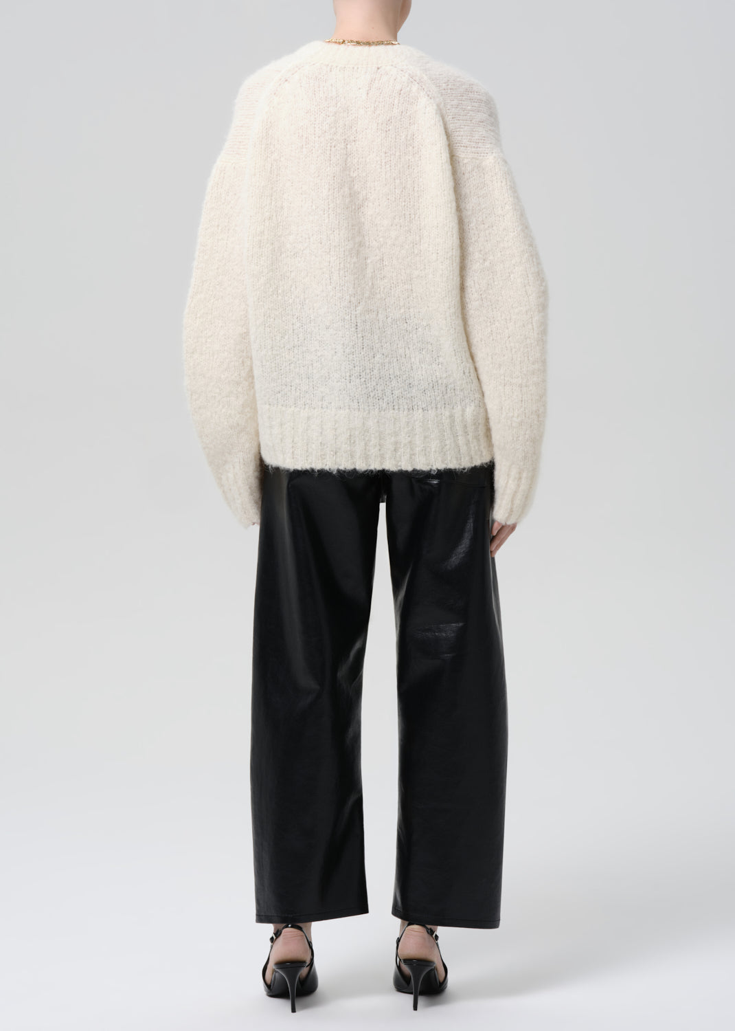 Person wearing a fluffy white sweater and black pants on a grey background