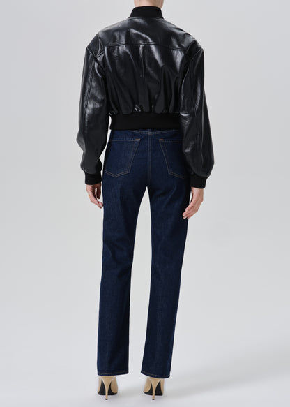 A model shown from the back wearing a black leather bomber jacket and dark blue straight-leg jeans, paired with beige high heels, against a grey background.