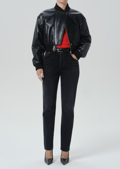 A model wearing a black leather bomber jacket, black skinny jeans, a red top, and black pointed-toe heels, photographed against a grey background.