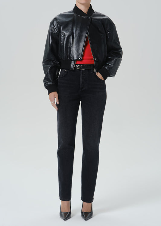 A model wearing a black leather bomber jacket, black skinny jeans, a red top, and black pointed-toe heels, photographed against a grey background.