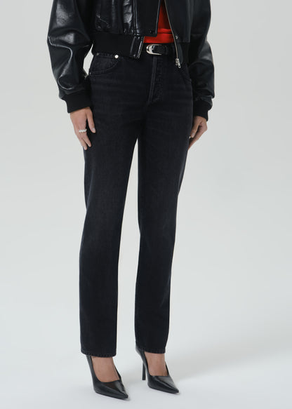A model wearing black slim-fit jeans with a black leather jacket, red top, and black pointed-toe heels, shown from the chest down on a grey background.
