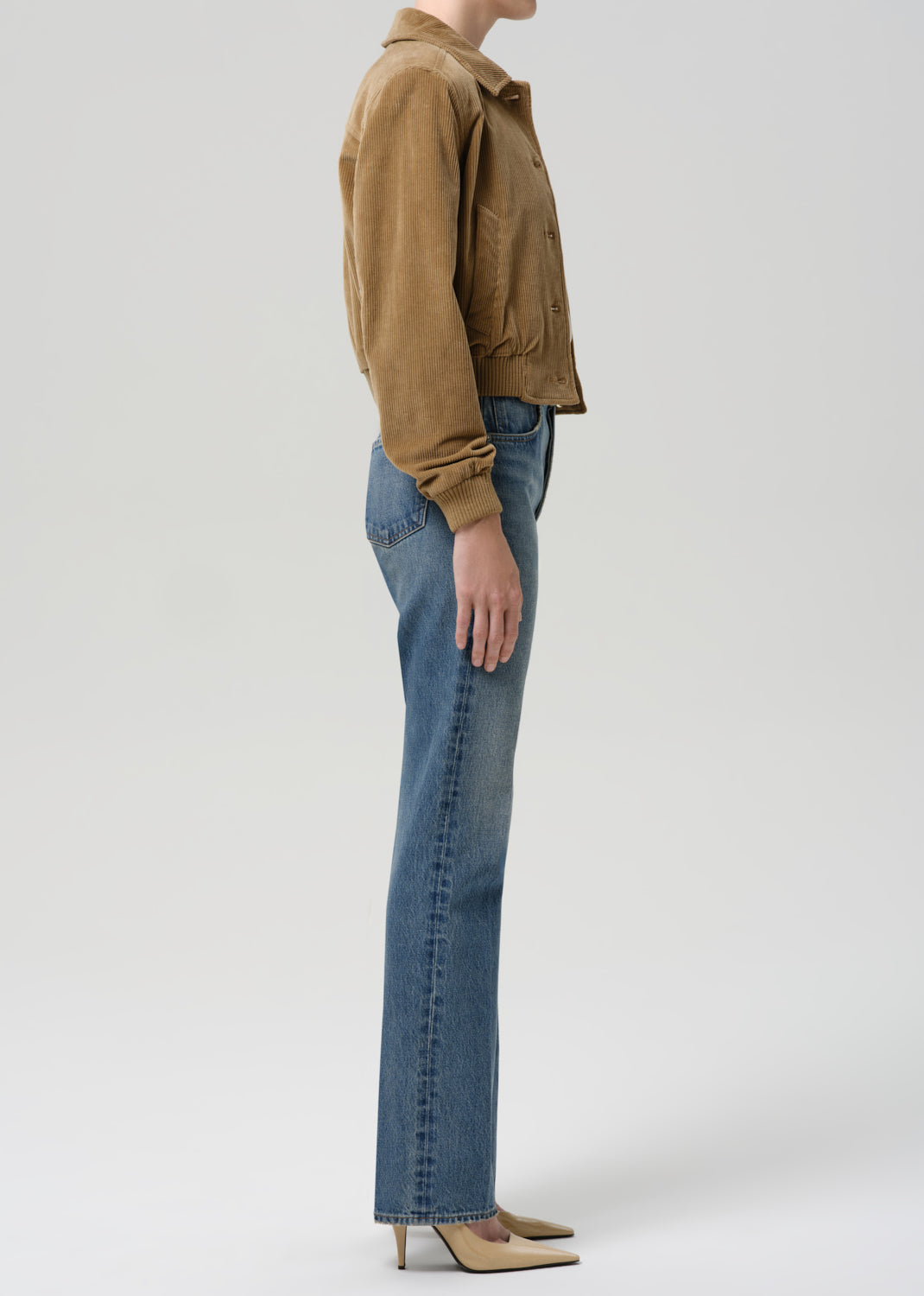 Person wearing a brown jacket and blue jeans on a grey background