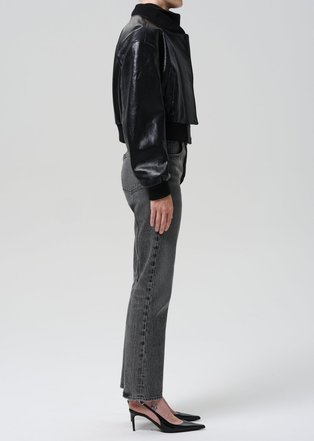 Person wearing a black leather jacket and gray pants on a grey background
