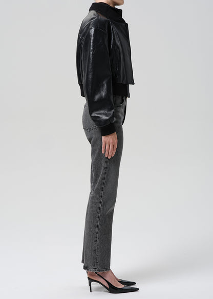 A model shown from the side wearing a black cropped faux-leather jacket, grey wide-leg jeans, and black pointed-toe heels against a grey background.