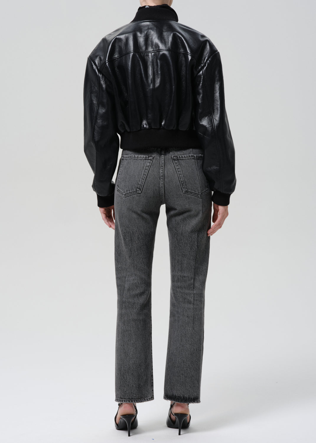 Person wearing a black leather jacket and gray jeans on a grey background