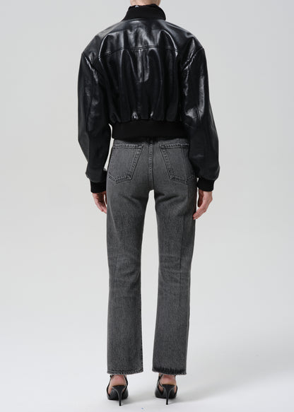 Person wearing a black leather jacket and gray jeans on a grey background