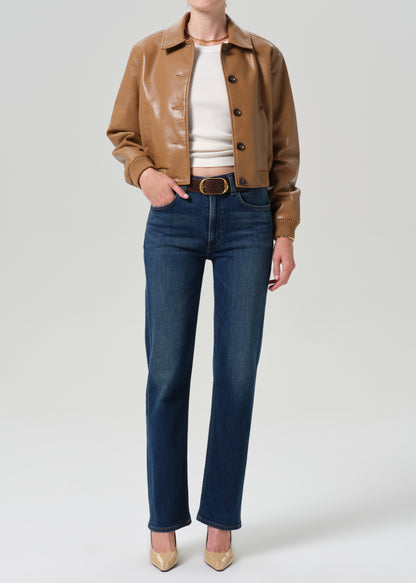 Person wearing a tan leather bomber jacket with dark indigo straight leg jeans on a grey background