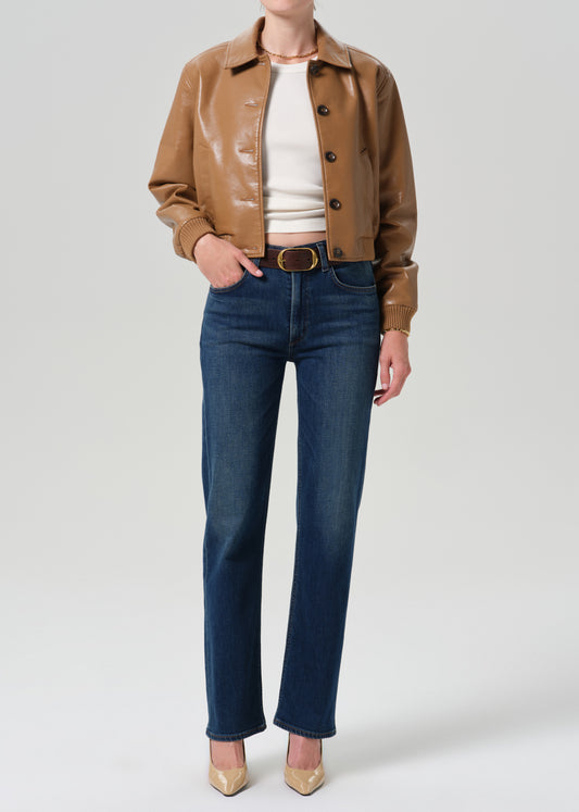 Person wearing a tan leather bomber jacket with dark indigo straight leg jeans on a grey background