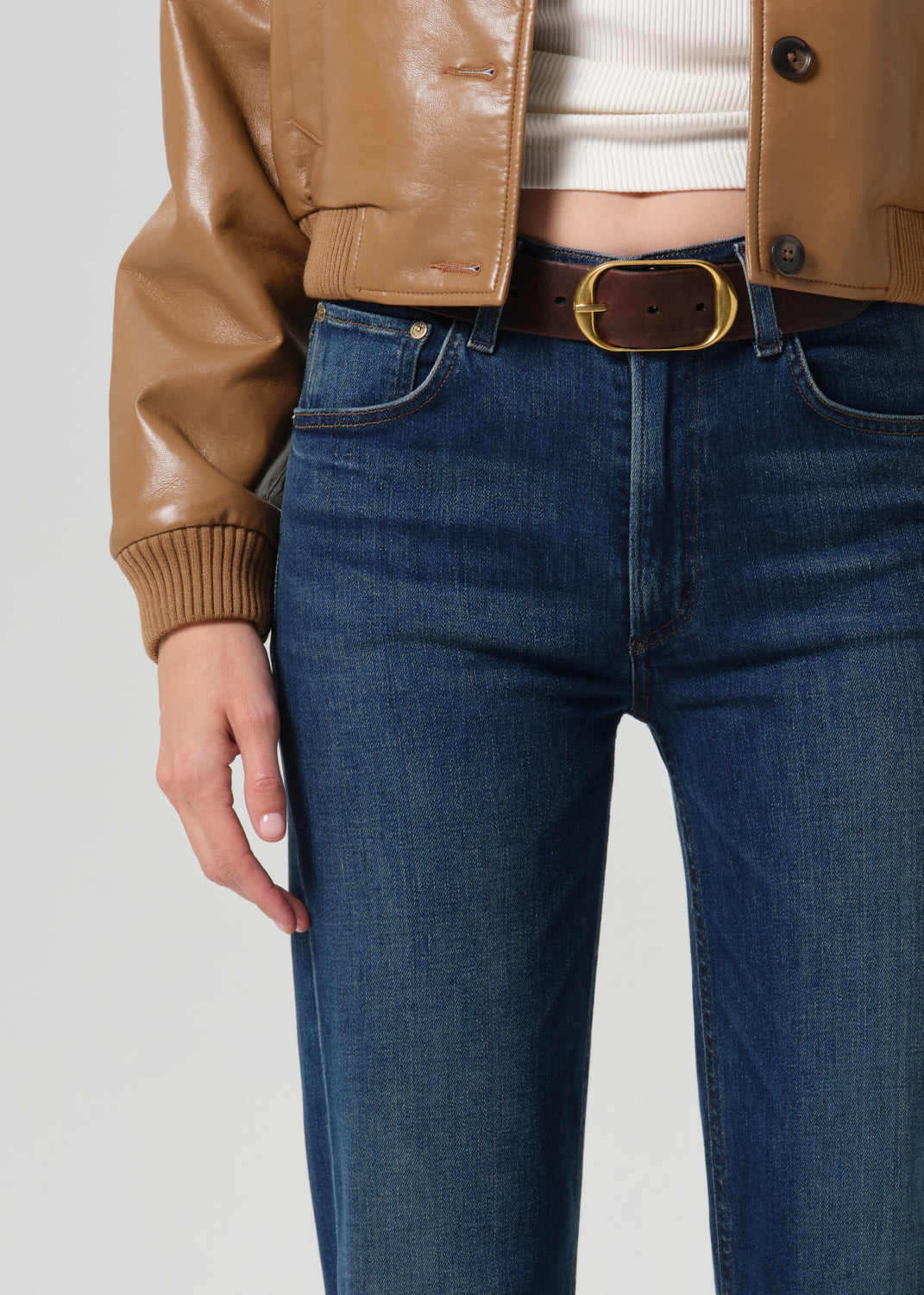 Close-up of dark indigo straight leg jeans with a tan leather bomber jacket on a grey background