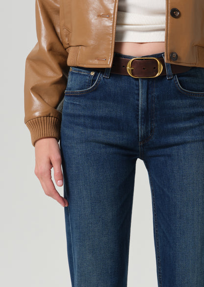 Close-up of dark indigo straight leg jeans with a tan leather bomber jacket on a grey background