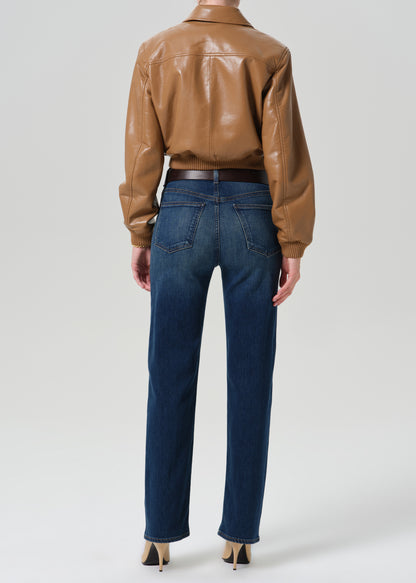 Person wearing a tan leather bomber jacket with dark indigo straight leg jeans viewed from the back on a grey background