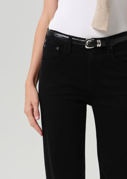 Close-up of black straight leg jeans with a white sleeveless knit top and sweater draped over the shoulders on a grey background