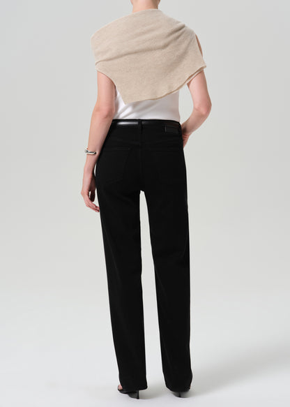 Person wearing a white sleeveless knit top with a sweater draped over the shoulders and black straight leg jeans viewed from the back on a grey background