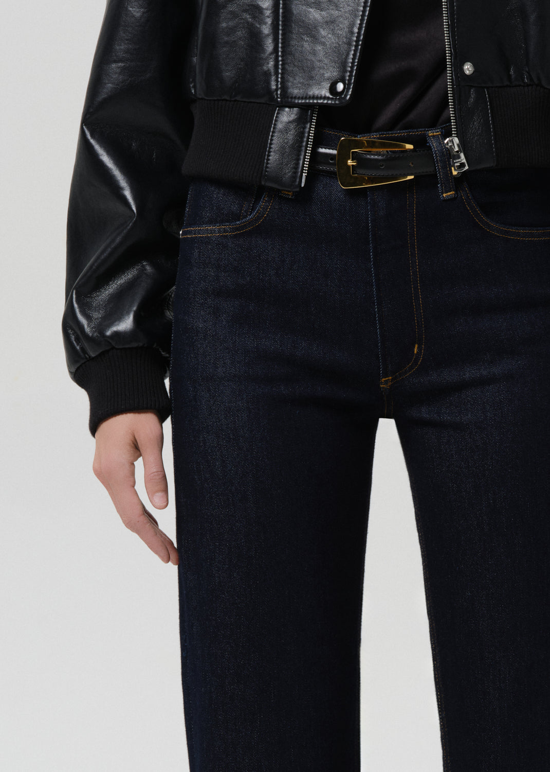 Person wearing a black leather jacket and dark jeans on a grey background