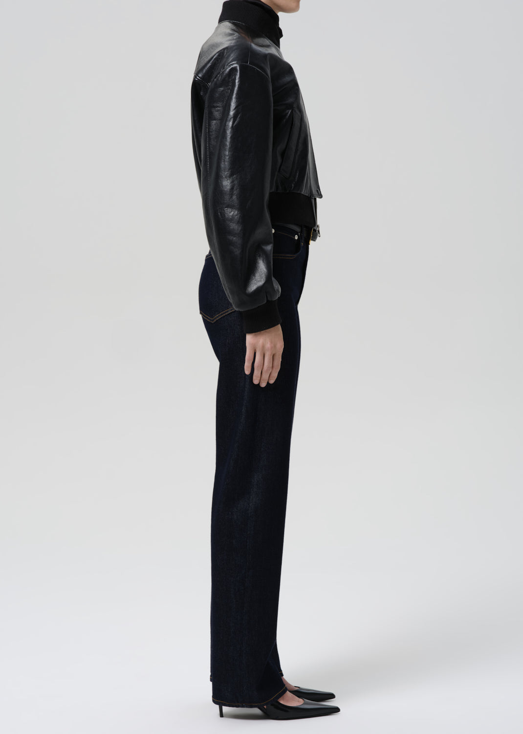 Person wearing a black leather jacket and pants on a grey background