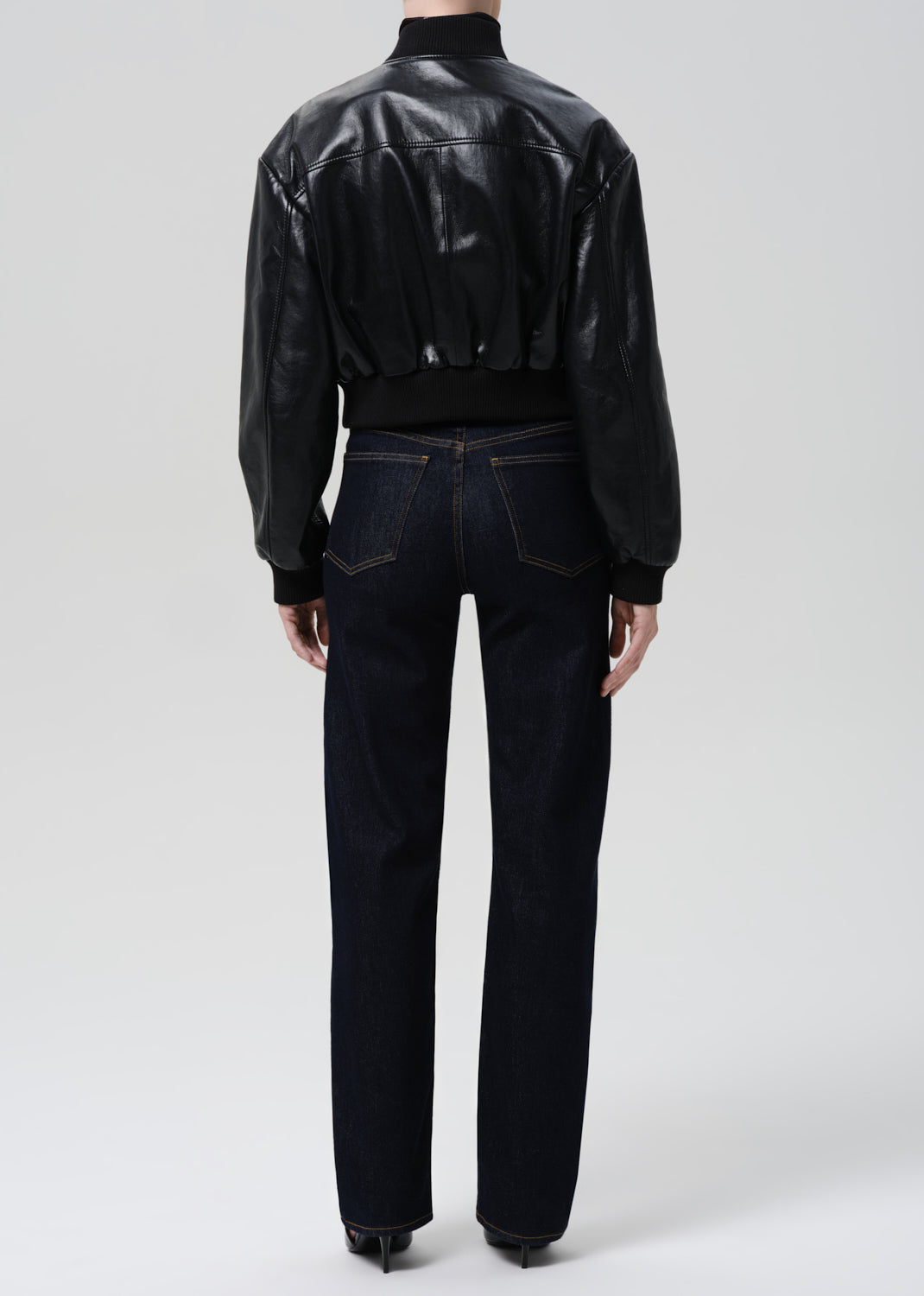 Person wearing a black leather jacket and dark jeans on a grey background