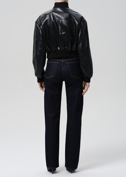 Person wearing a black leather jacket and dark jeans on a grey background