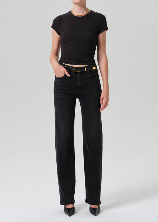 A model wearing a black short-sleeve crop top and black wide-leg jeans with a black belt, standing against a grey background.