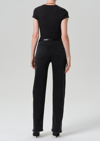 Rear view of a model wearing black high-waisted straight-leg jeans, a black short-sleeve top, and black heels against a grey background.