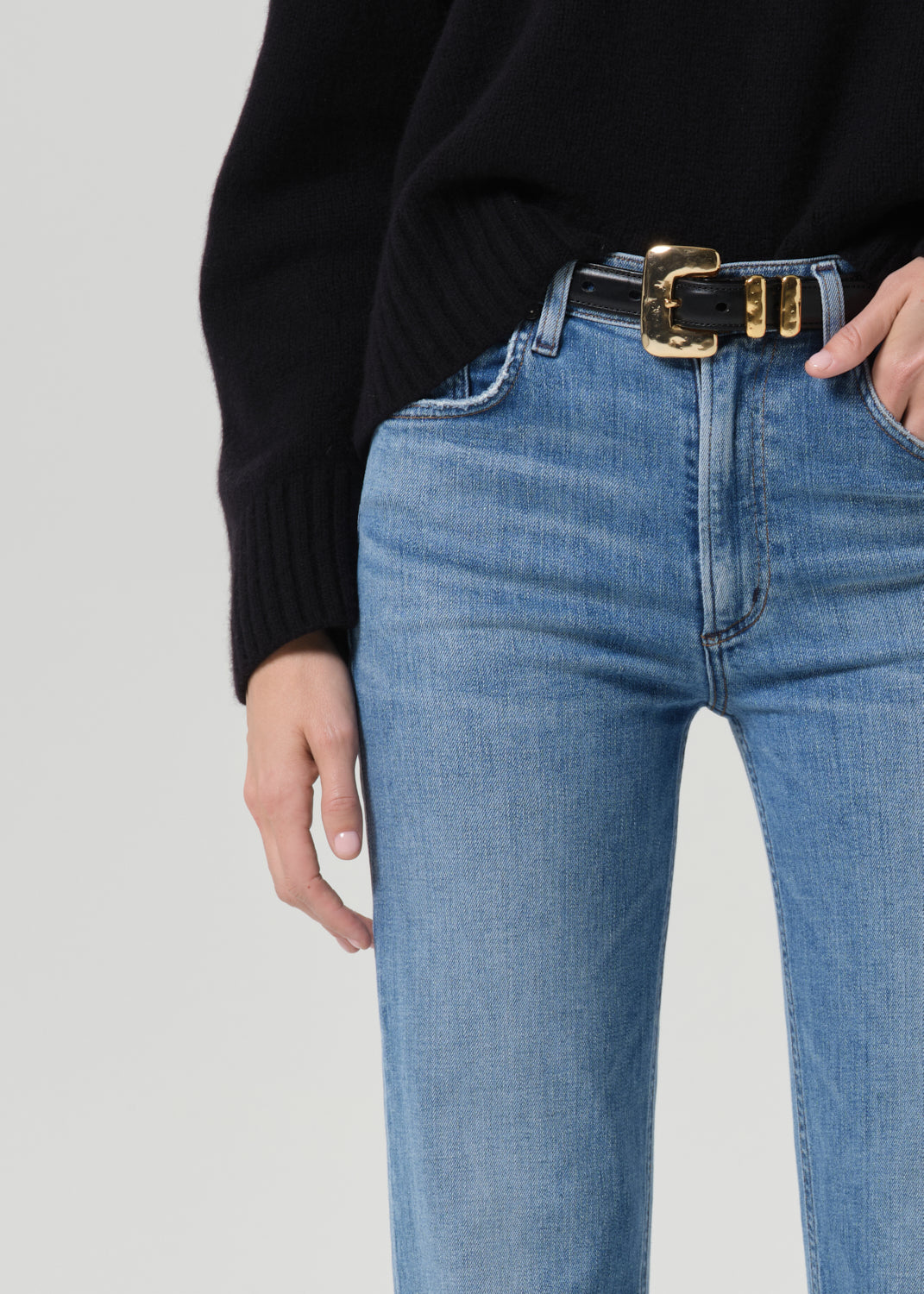 Close-up of light wash straight leg jeans with a black crewneck sweater on a grey background