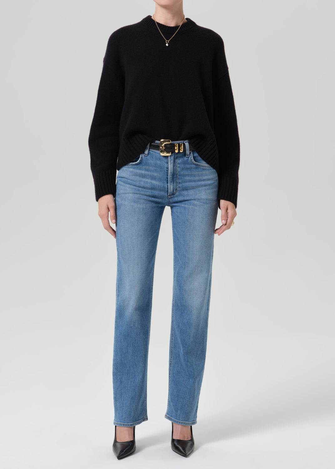 Person wearing a black crewneck sweater with light wash straight leg jeans on a grey background