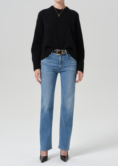 Person wearing a black crewneck sweater with light wash straight leg jeans on a grey background