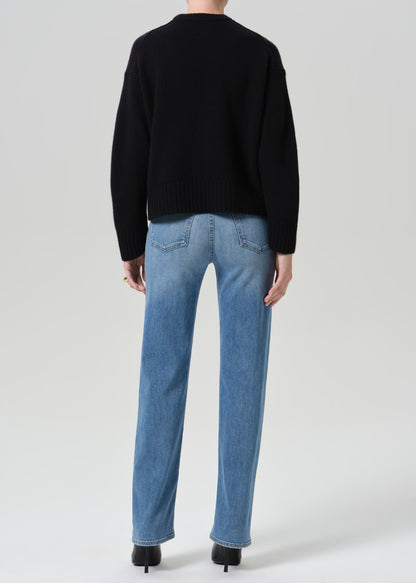 Person wearing a black crewneck sweater with light wash straight leg jeans viewed from the back on a grey background