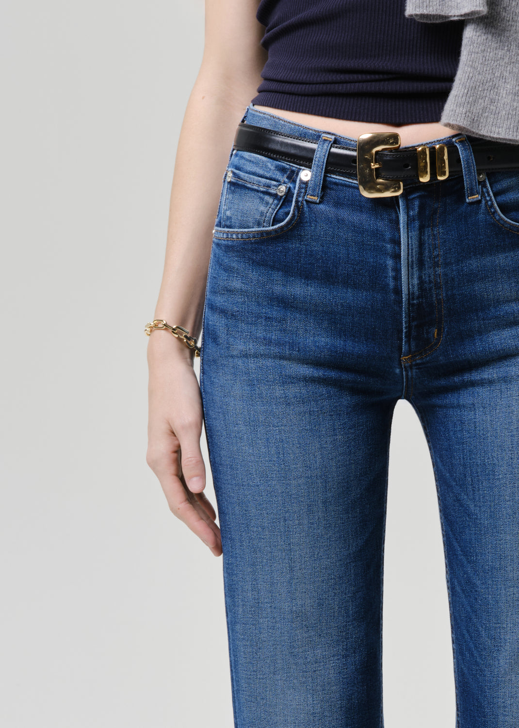 Person wearing blue jeans with a black belt on a grey background